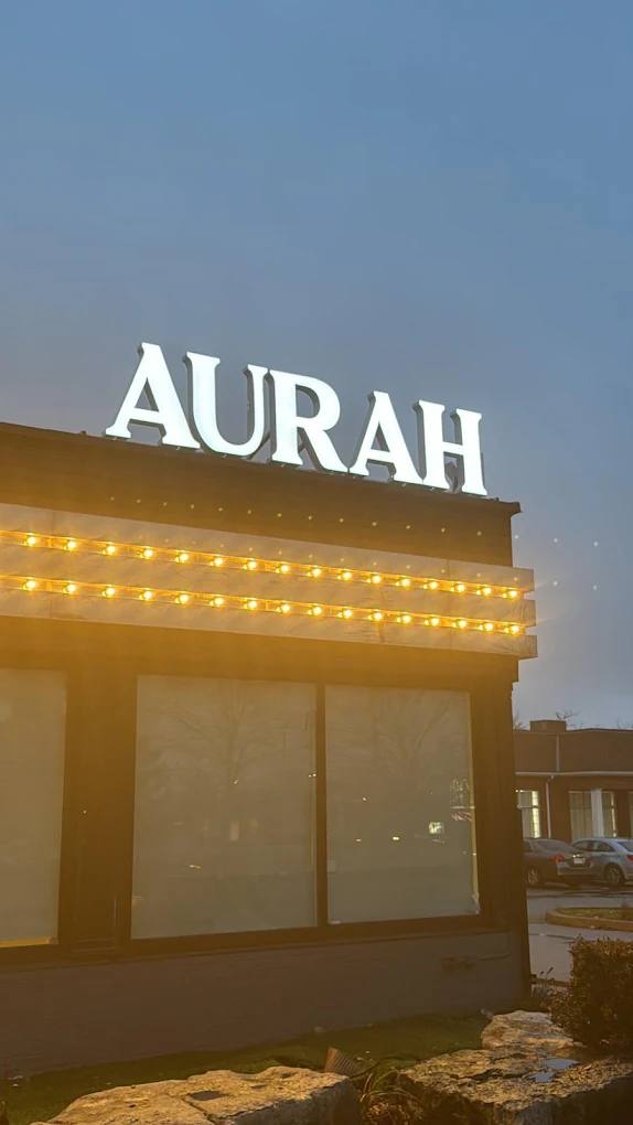 Illuminated white AURAH letters on a building roofline at dusk